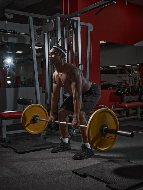 Sports powerful african american guy squats with barbell during strength training in gym weight