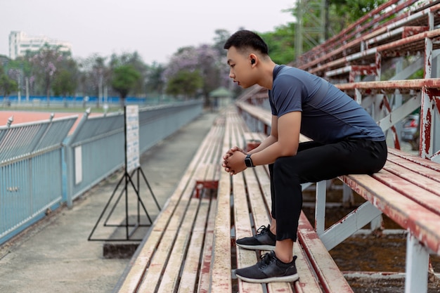 Concetto di sport e ricreazione un giovane maschio seduto su una tribuna al confine di uno staduim.
