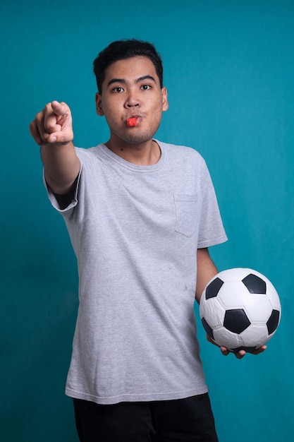 Sports referee blowing a whistle and pointing with finger isolated on blue background