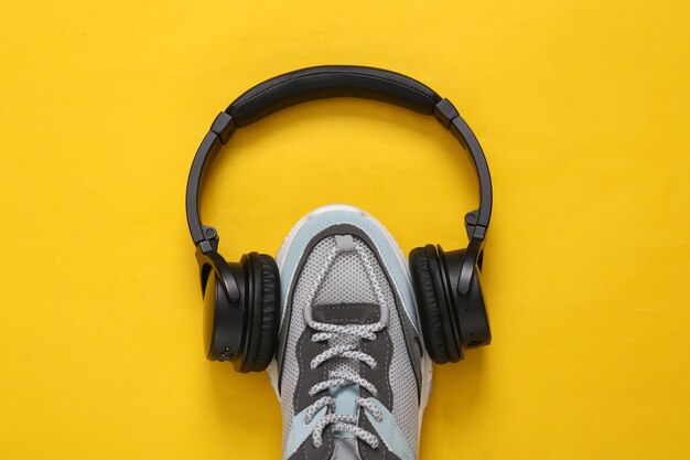 Sports shoe with headphones on yellow background Fitness concept Top view Minimalism