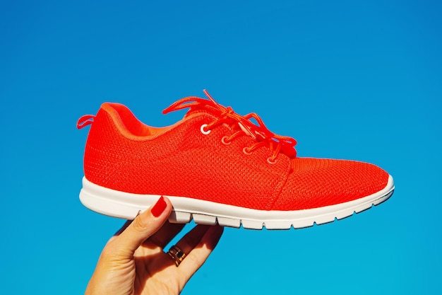 Sports shoes sneakers on blue sky background sports in the open\
air woman hand holding orange sneakers fitness and health