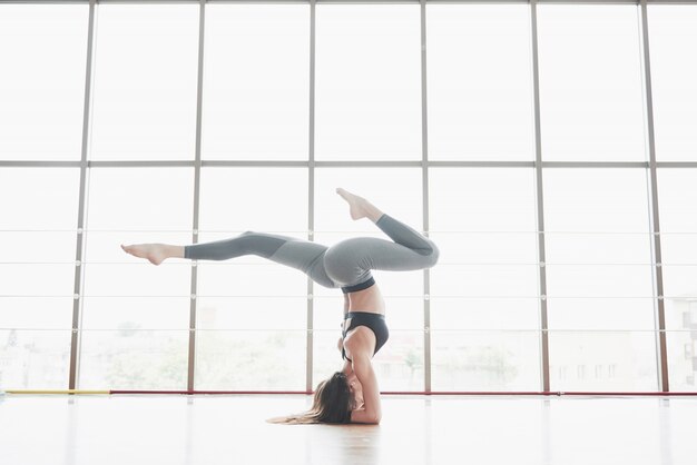 Una donna sportiva che sta facendo lezioni di yoga, allungando le gambe vicino alla grande finestra