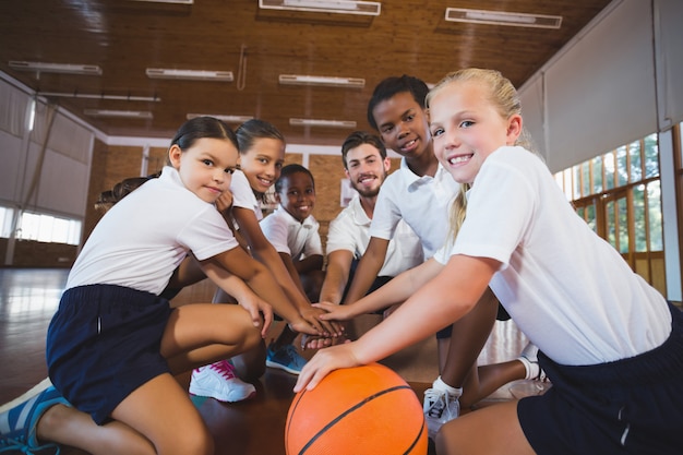 Photo sports teacher and school kids forming hand stack in basketball court