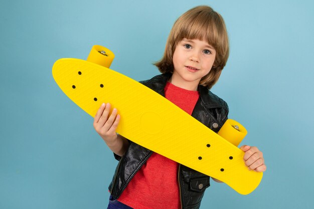 Sports teenager boy in red t-shirt and black jacket with yellow penny on blue wall