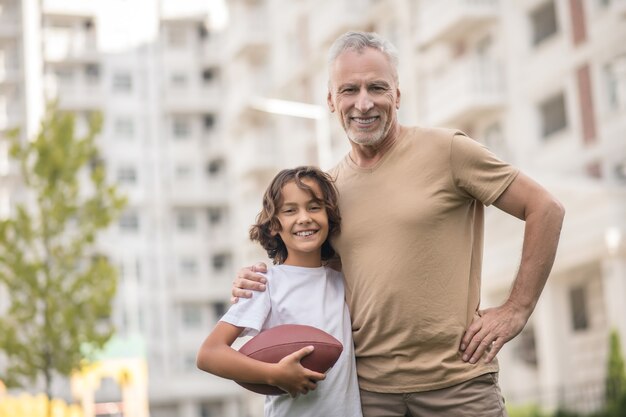 Sports time. Dark-haired boy in a white tshirt playing ball with his dad