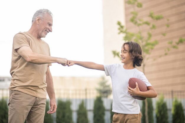 Sports time. Dark-haired boy in a white tshirt playing ball with his dad