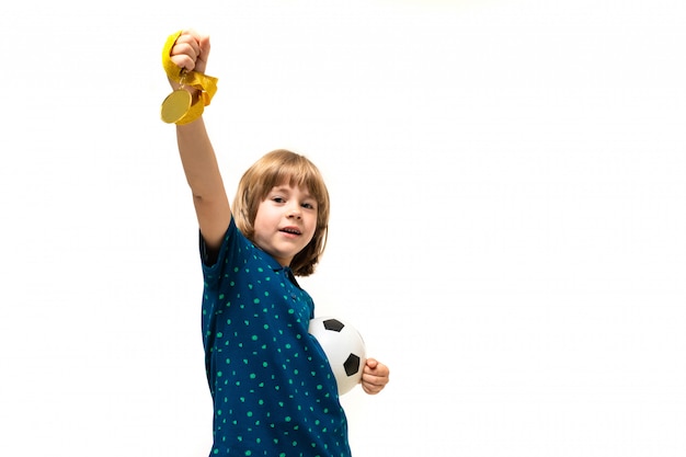 Sports winner boy holding a soccer ball and a medal in his hands on a white