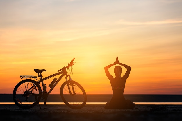 The sports woman doing yoga at sunrise on the sea beach