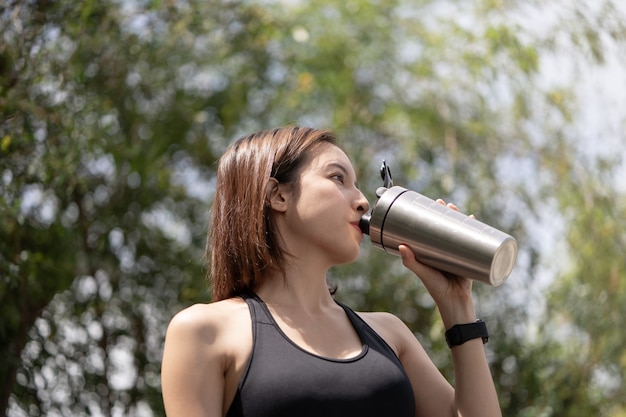 La donna sportiva beve il frullato proteico dallo shaker per bottiglie in acciaio inossidabile