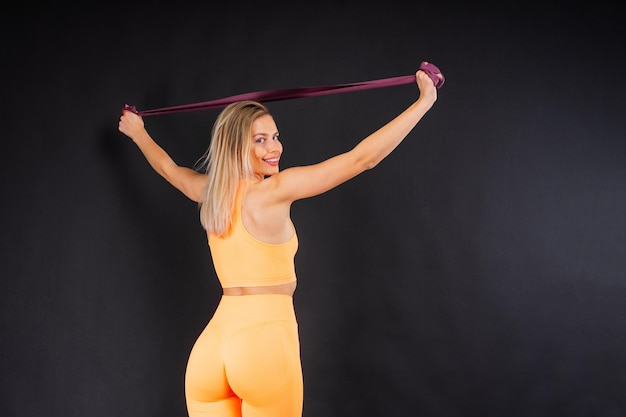 Sports woman in fashion sportswear exercising with elastic band in studio