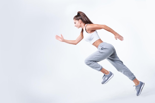 Sports woman runner on a white background Photo of an attractive woman in fashionable sportswear Dynamic movement Side view Sports and healthy lifestyle