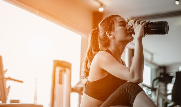 The sports young woman drinks protein in a shaker in a gym. Sports 
concept