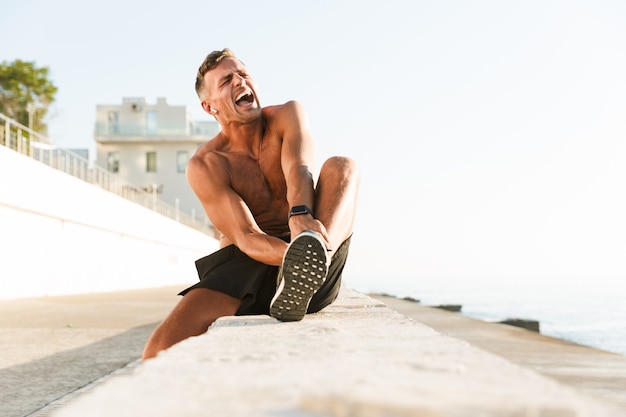 Sportsman on the beach touching his leg because of painful injury.