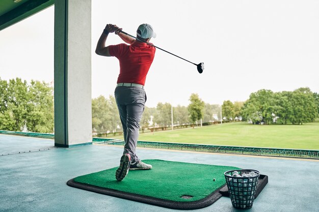 Photo sportsman in a cap perfecting backswings on the golf hitting mat