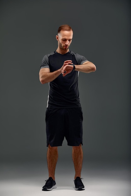 Sportsman checking heart rate on fitness tracker when training studio shot on gray background