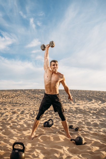 Спортсмен делает упражнения с весами в пустыне в солнечный день. Сильная мотивация в спорте, силовые тренировки на свежем воздухе