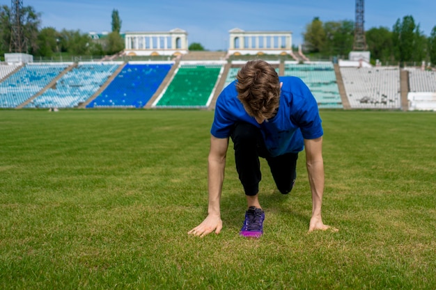 Спортсмен делает упражнения на растяжку на стадионе перед летними тренировками