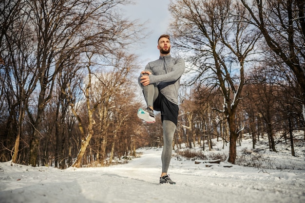 스포츠맨은 스트레칭 운동을 하고 눈 덮인 겨울 날 자연에서 달릴 준비를 합니다. 겨울 피트니스, 스포츠, 추운 날씨