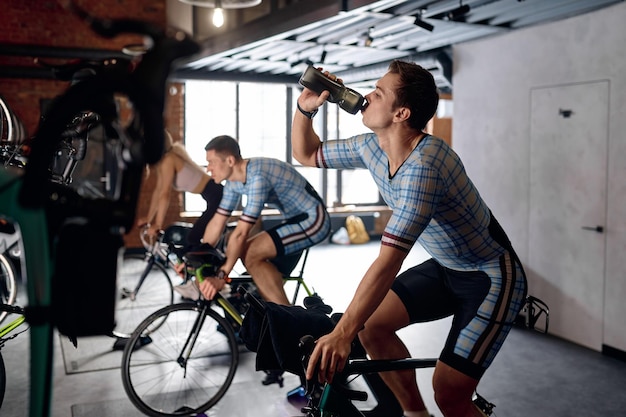 Photo sportsman drinking water training on stationary bike