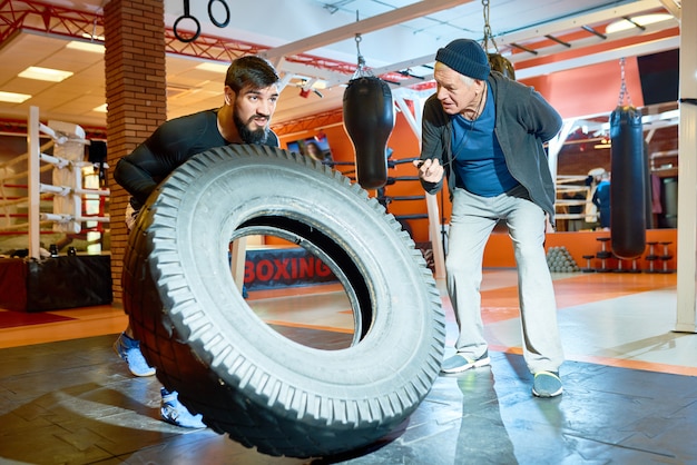 Sportsman flipping tyre with coach near