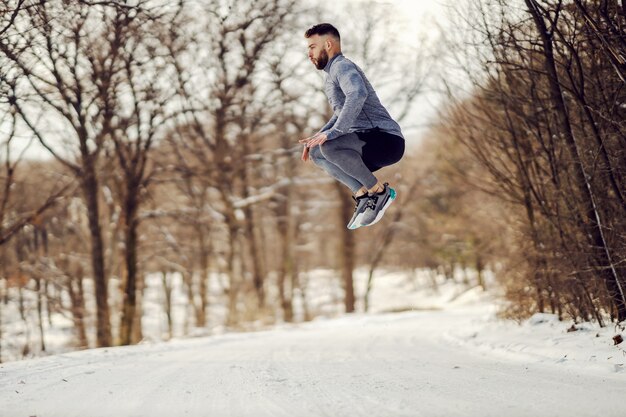 雪の降る冬の日に自然の中で高くジャンプするスポーツマン。健康的な習慣、ウィンタースポーツ