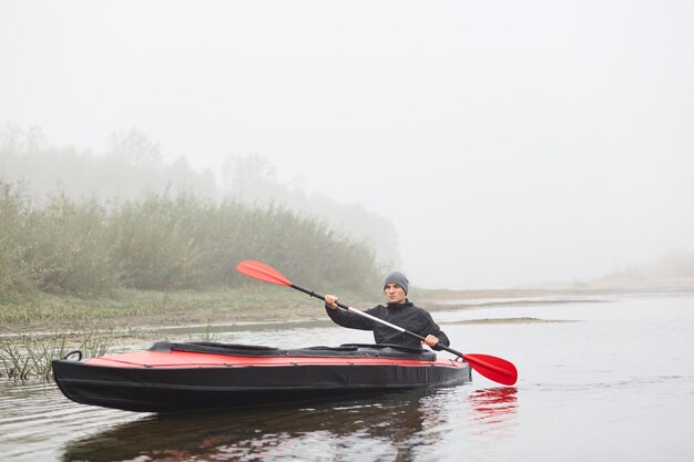 Sportsman in kayak, padding in foggy river, spending his free time outdoors, doing water sport, posing with oar in hands