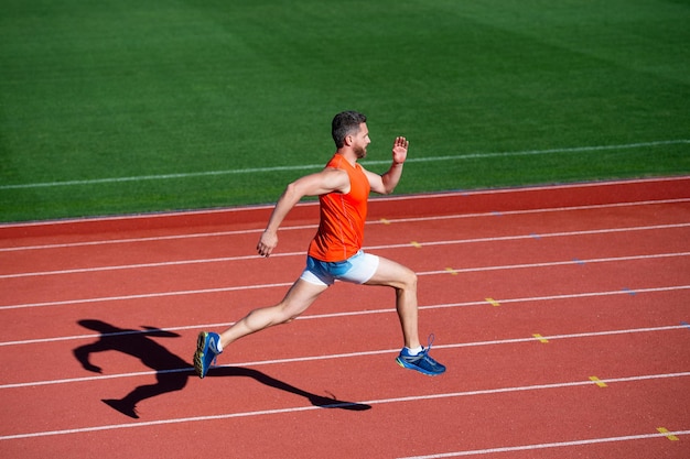 スポーツウェアのスポーツマンの男は、ランニングトラックのエネルギーで全力疾走を実行します