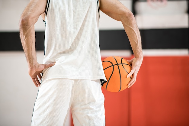 スポーツマン。手に大きなオレンジ色のボールを保持している白いスポーツウェアの男