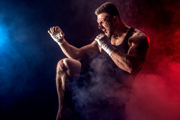 Sportsman muay thai boxer fighting on black wall with smoke.