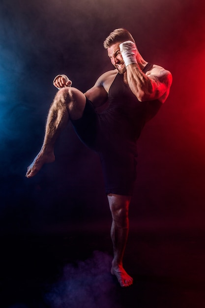 Sportsman muay thai boxer fighting on black wall with smoke.