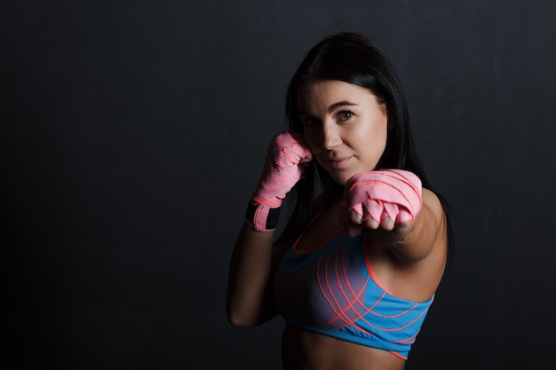 Sportsman muay thai woman boxer posing in training studio at black background.