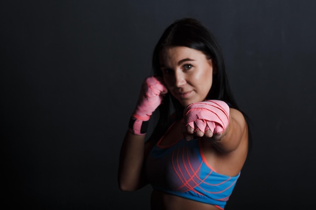 Sportsman muay thai woman boxer posing in training studio at black background