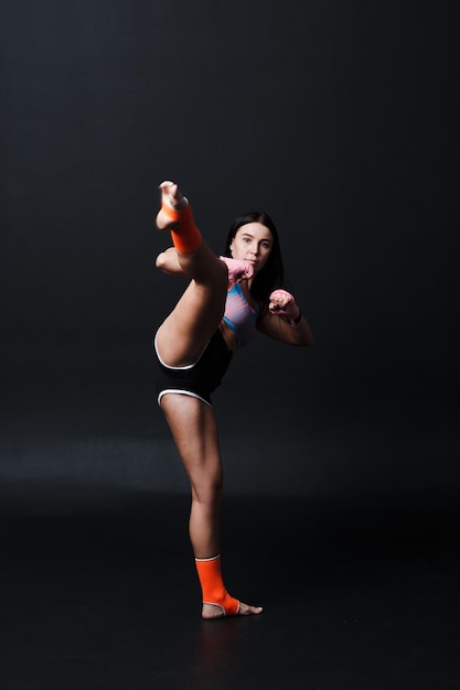 Sportsman muay thai woman boxer posing in training studio at black background