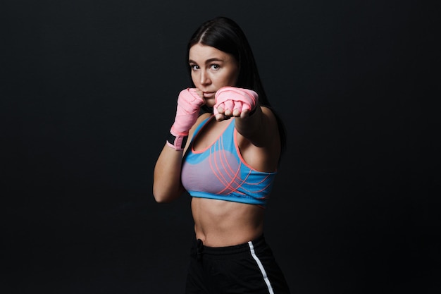 Sportsman muay thai woman boxer posing in training studio at black background