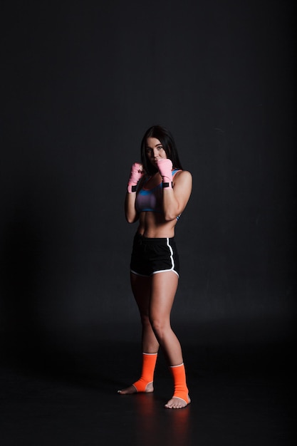 스포츠맨 무에타이 여성 권투 선수가 검정색 배경에서 훈련 스튜디오에서 포즈를 취하고 있습니다.
