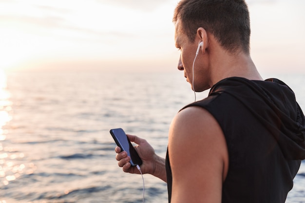 Sportsman outdoors at the beach listening music with earphones.