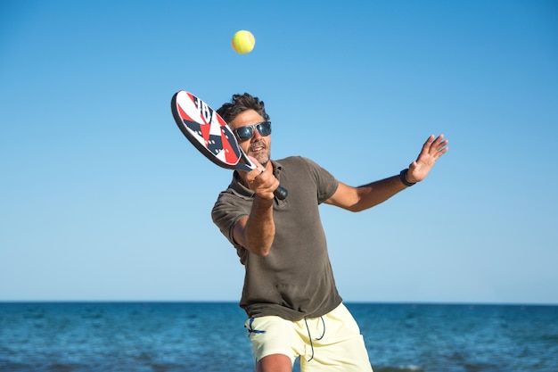 Photo sportsman playing tennis on the beach with blue sky background. paddle tennis player
