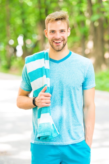 Sportsman promoting a healthy lifestyle. Happy sportsman or trainer on summer day. Fit sportsman using towel during training outdoor. Handsome sportsman or sports coach smiling on natural landscape.