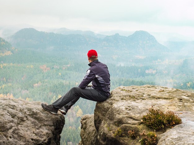 Photo sportsman relaxing at rocky edge in mountains enjoy amazing view into morning hilly landscape