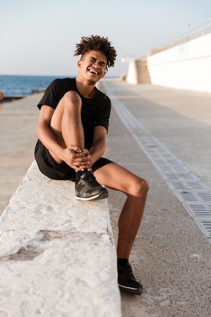 Sportsman sitting with pain in leg outdoors on the beach