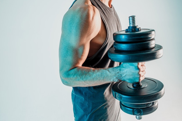 Sportsman training biceps muscles with dumbbell. Man wear sports uniform. Isolated on turquoise background. Studio shoot