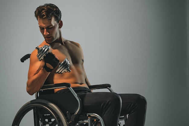 The sportsman in wheelchair works with dumbbell