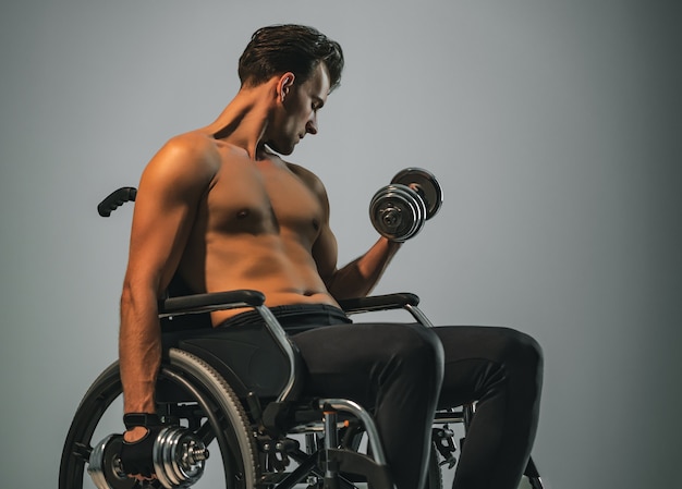 The sportsman in wheelchair works with dumbbell