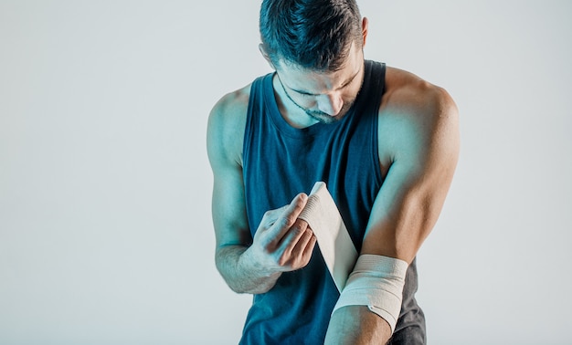 Photo sportsman wrapping medical bandage on hand. young bearded european man wear sports uniform. concept of sports injury. isolated on turquoise background. studio shoot. copy space