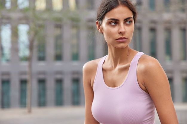 Sportiva in maglietta casual distoglie lo sguardo pensieroso cammina all'aperto durante le pose diurne su un edificio sfocato