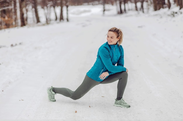 冬の雪の上で自然にしゃがみ、ウォームアップ運動をしているスポーツ選手。自然、森、冬のフィットネス、健康的なライフスタイル