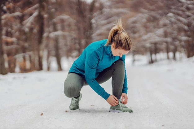 Sportswoman crouching on snow in nature at winter and tying shoelace