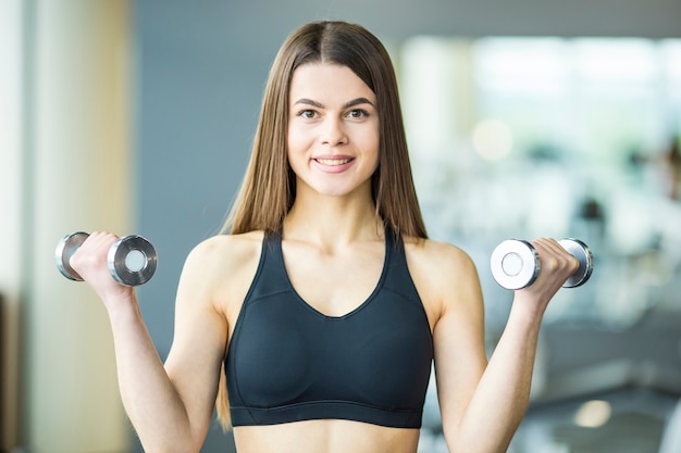 The sportswoman doing exercise with dumbbells in the gym