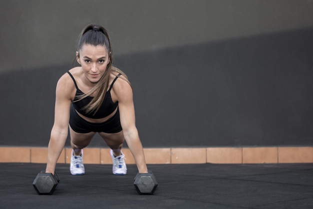 Sportswoman doing plank on dumbbells