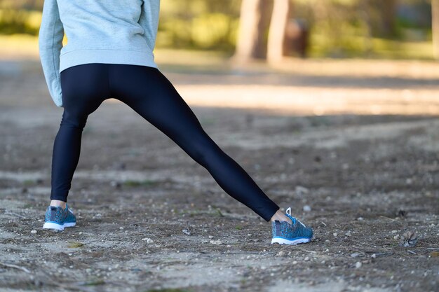 Sportswoman doing stretching exercises seen from behind in the urban forest black leggings